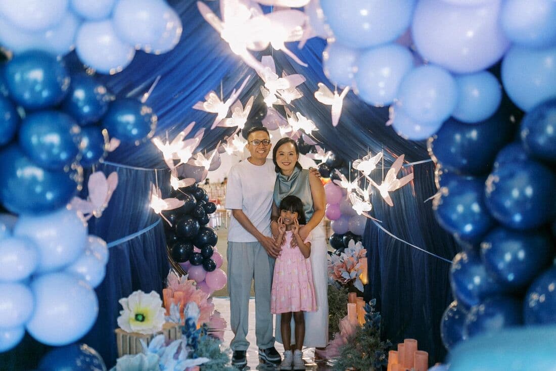 A family under a blue balloon arch with sparklers