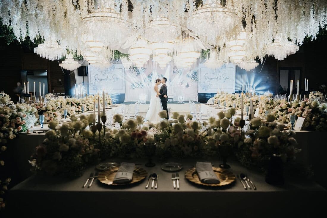A couple on a floral stage above a long banquet table