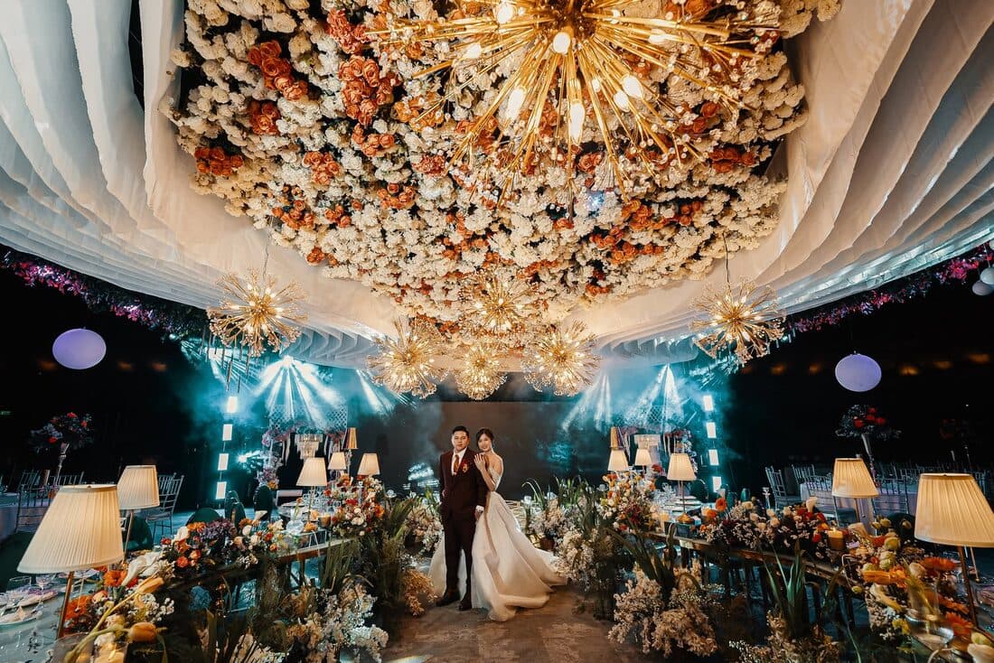 The couple on stage under a chandelier of flowers