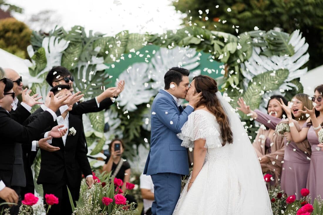 A couple kissing at the end of the aisle as guests cheer