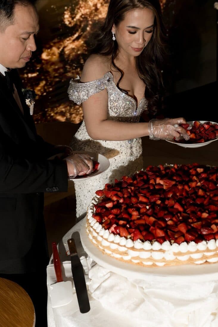 The couple cutting a cake heaped with strawberries